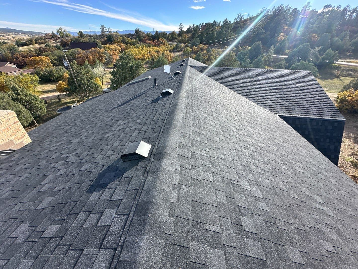 Aerial view of completed charcoal asphalt shingle roof installation with Colorado mountain backdrop