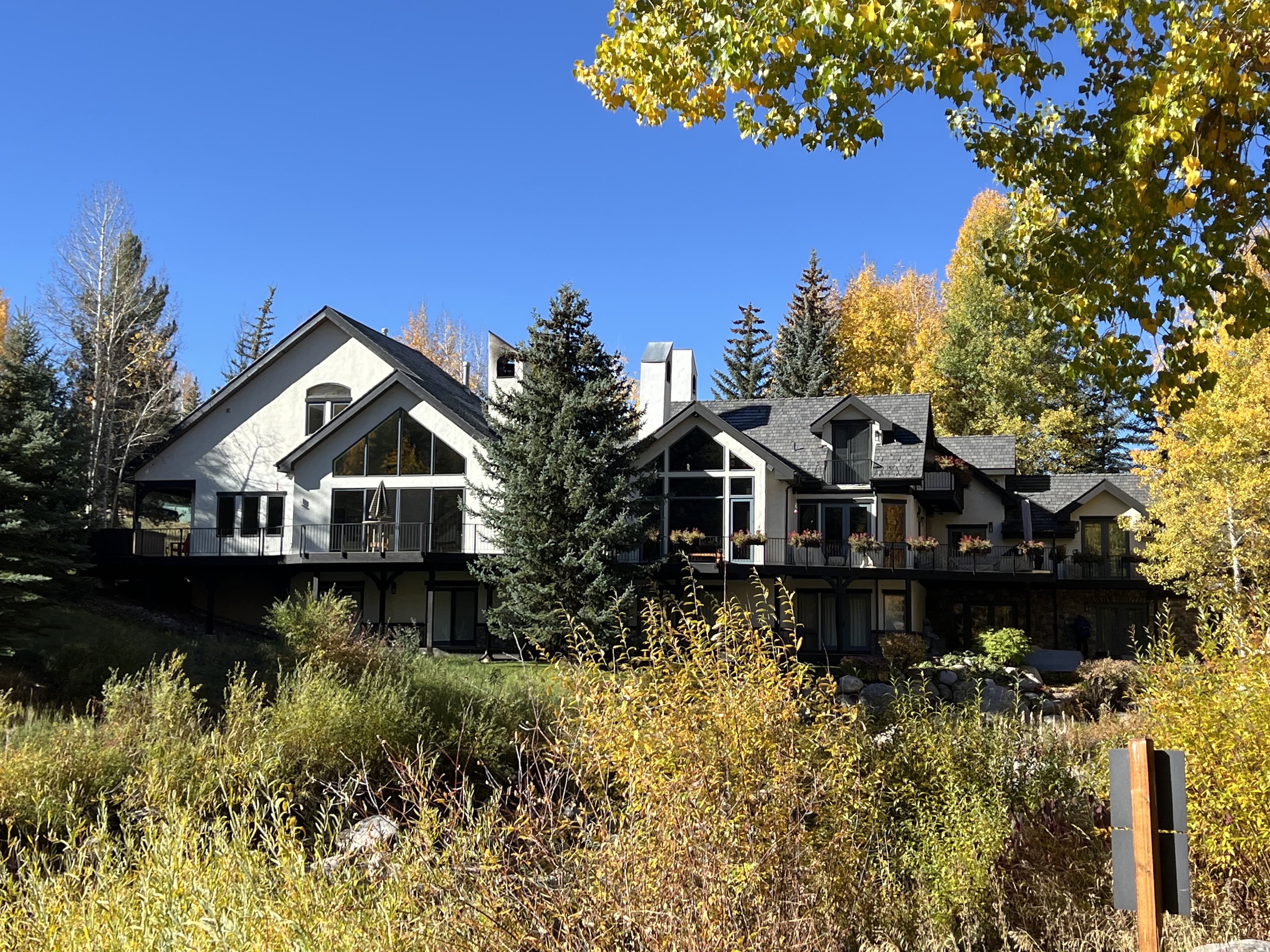 Large Colorado mountain home exterior with dark architectural shingle roof surrounded by fall foliage