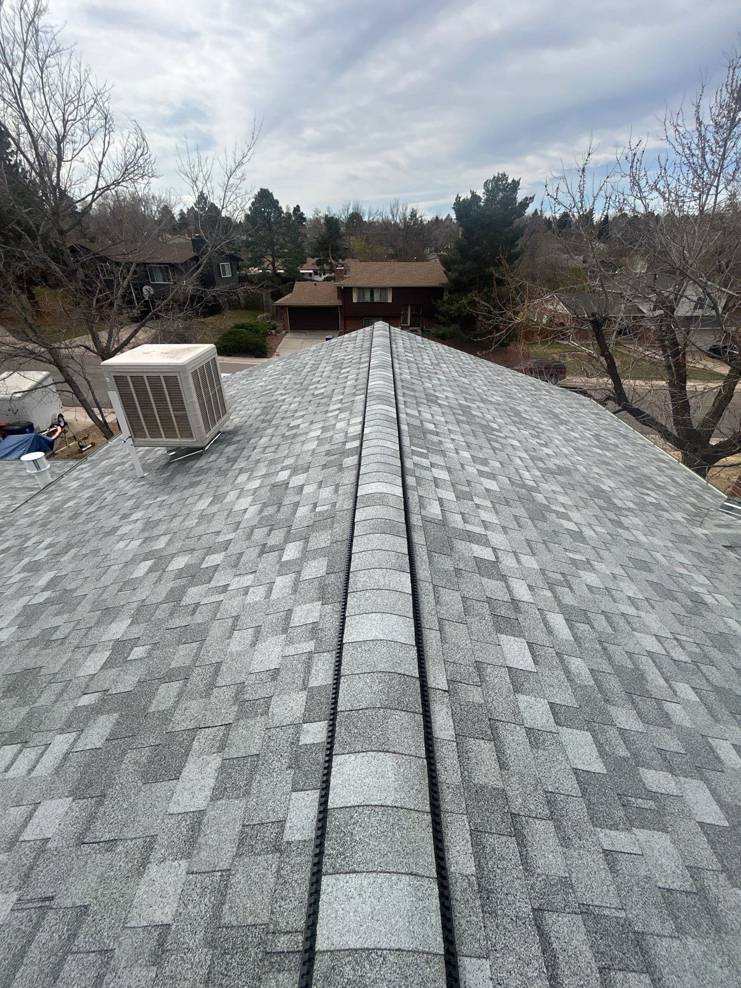 Completed gray architectural shingle roof replacement with ridge cap and rooftop HVAC unit, aerial view in Centennial CO