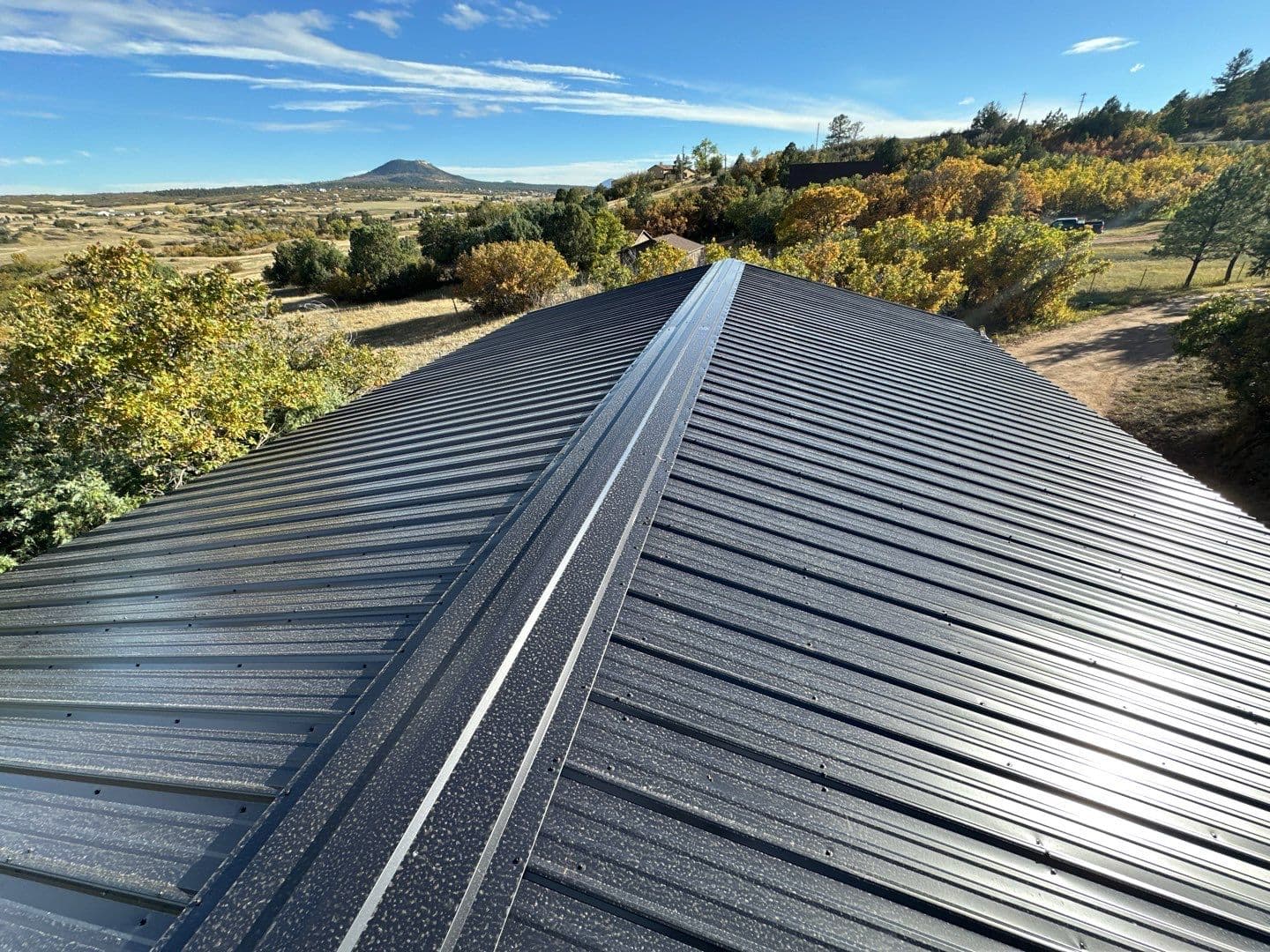 Standing seam metal roof installation in dark charcoal with panoramic Colorado mountain and fall foliage views